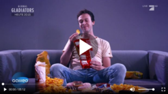 Eine Person sitzt auf einem Sofa, hält eine Chipstüte und ist umgeben von verschiedenen Snacks und Donuts auf dem Tisch.