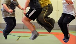 Vier Kinder in Freizeitkleidung springen synchron über ein gespanntes Seil.