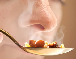 Nase einer Person in der Nähe eines Löffels mit dampfendem Essen, das aus verschiedenen Zutaten besteht.